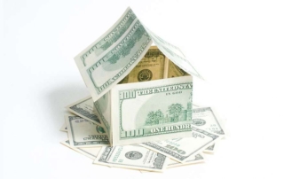 House made of one hundred dollar bills and sitting on a pile of one hundred dollar bills.