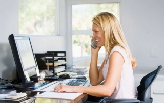 Woman in home office with computer talks to client on phone