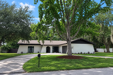 - Graystone Investment Group Single-story white house with a curved driveway, a well-kept front yard, and a tall tree centered in the lawn.
