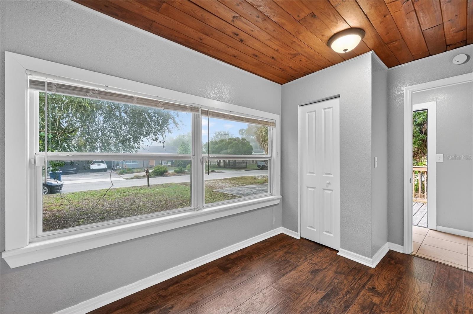 1908-2 - Graystone Investment Group Room with wood-paneled ceiling, large double window, gray walls, and dark hardwood flooring. A white closet door is visible to the right.
