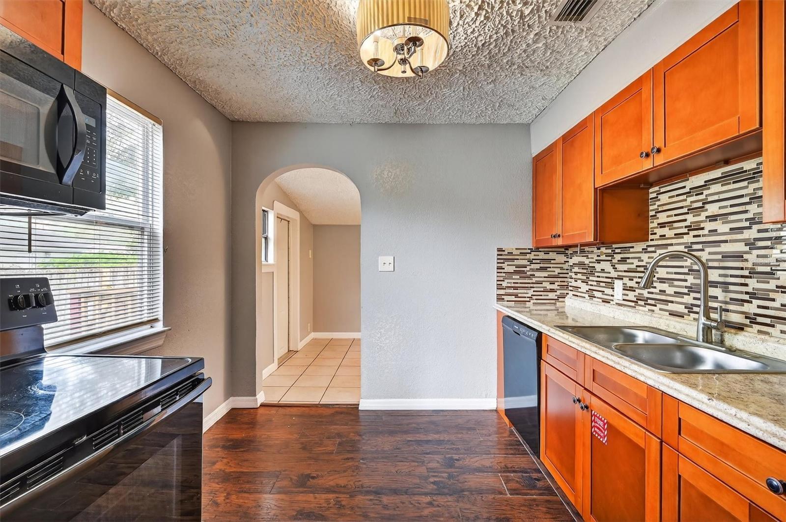 1908-8 - Graystone Investment Group Modern kitchen with orange wooden cabinets, granite counter, mosaic tile backsplash, and stainless steel sink on dark hardwood floors in a U-shape layout.