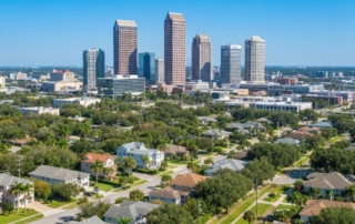 City skyline with tall office buildings rising over a suburban neighborhood on a sunny day with palm trees in the foreground