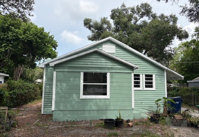 - Graystone Investment Group Front view of a small mint-green house with white trim, dirt yard, and potted plants under a partly cloudy sky.