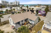 IMG_5462 - Graystone Investment Group Aerial view of a beachside neighborhood with palm trees, a beige house with a brown roof in the foreground, and the ocean in the distance.