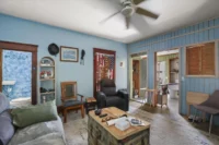 IMG_5472 - Graystone Investment Group Cozy living room with light blue walls, a ceiling fan, and mixed furniture including a black recliner and wooden chairs.