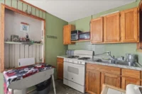 IMG_5473 - Graystone Investment Group Small kitchen corner with wooden cabinets, a white gas stove, and a double sink against light-green walls