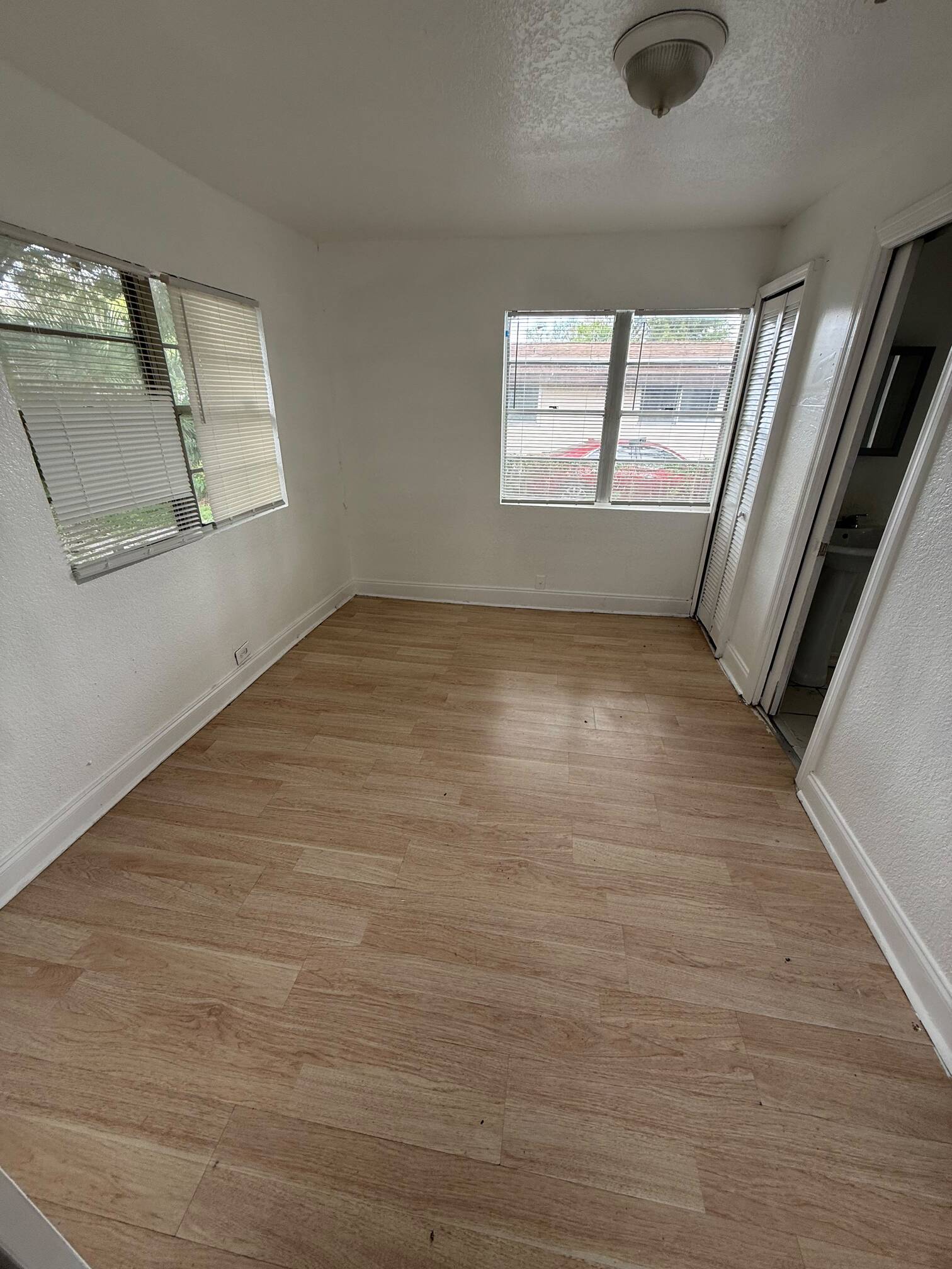 WhatsApp Image 2026-07-23 at 61615 PM - Graystone Investment Group Small empty sunlit room with light wood floor, white walls, and three windows with blinds.