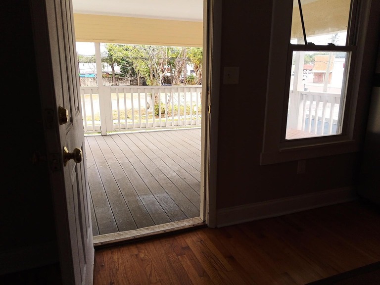 imgi_686_766f38e7aec17c313d9259d35d65adfe-uncropped_scaled_within_1536_1152 - Graystone Investment Group Interior room with wooden floor and an open door leading to a covered porch with a white railing and wooden deck outside, sunlight streaming in.