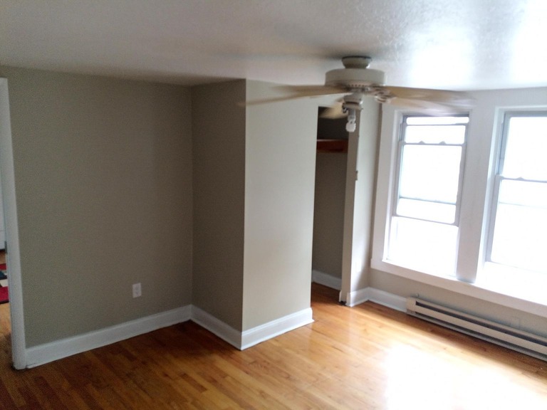 imgi_694_db28757c74d3e4cb5db1e31c96ce0887-uncropped_scaled_within_1536_1152 - Graystone Investment Group Empty living room with hardwood floors, beige walls, and a ceiling fan under natural light from large windows.
